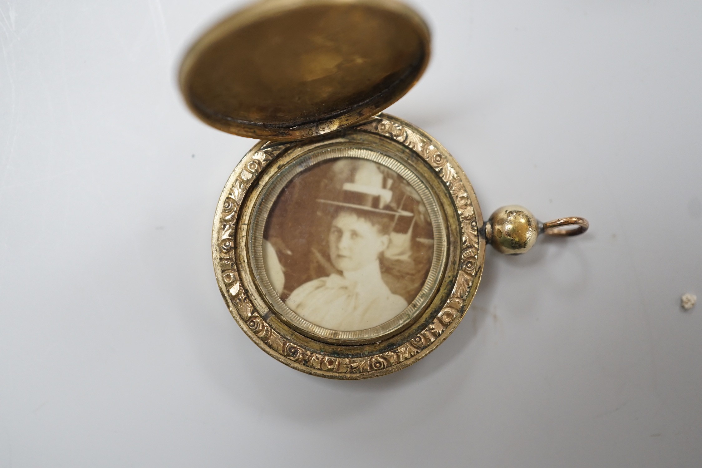 A Victorian yellow metal and seed pearl mounted black onyx oval pendant locket, with enamelled bale, overall 53mm and an engraved gold plated circular pendant locket.